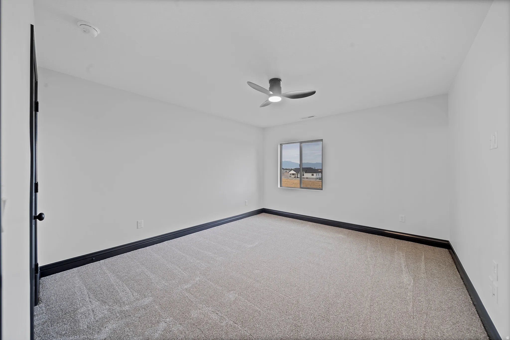 Light-filled room featuring neutral-toned carpeting and a modern ceiling fan
