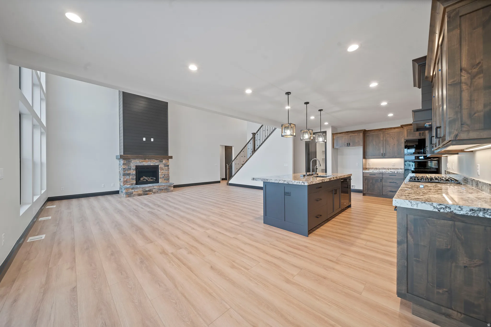 Open concept living space featuring a stone-clad fireplace with dark wood mantel, high ceilings, and wood-finish flooring