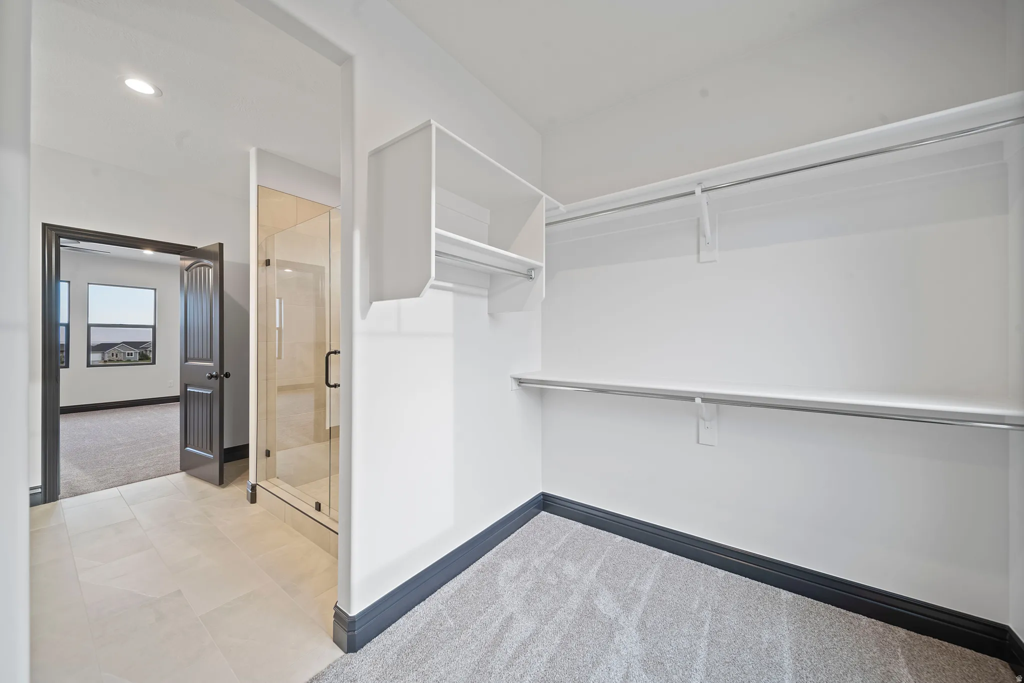 Spacious walk-in closet featuring white built-in shelving, hanging rods, and light gray carpet flooring