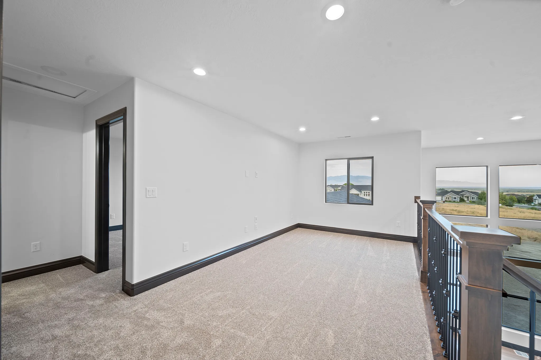 Upper-level landing featuring neutral carpeting, recessed lighting, and a dark wood and wrought iron railing