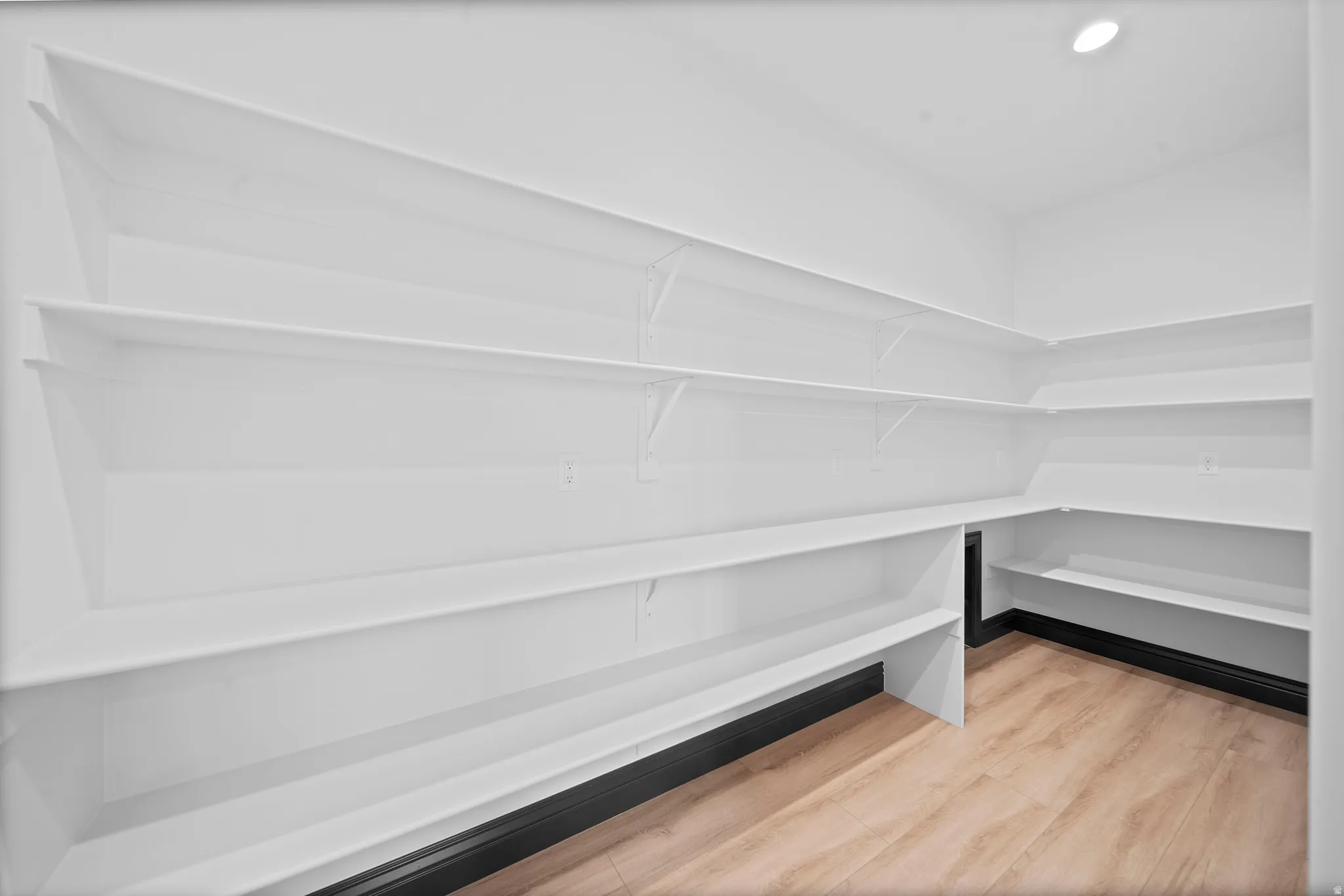 Spacious pantry featuring extensive white shelving, wood-finish flooring, recessed lighting, and a dark baseboard trim