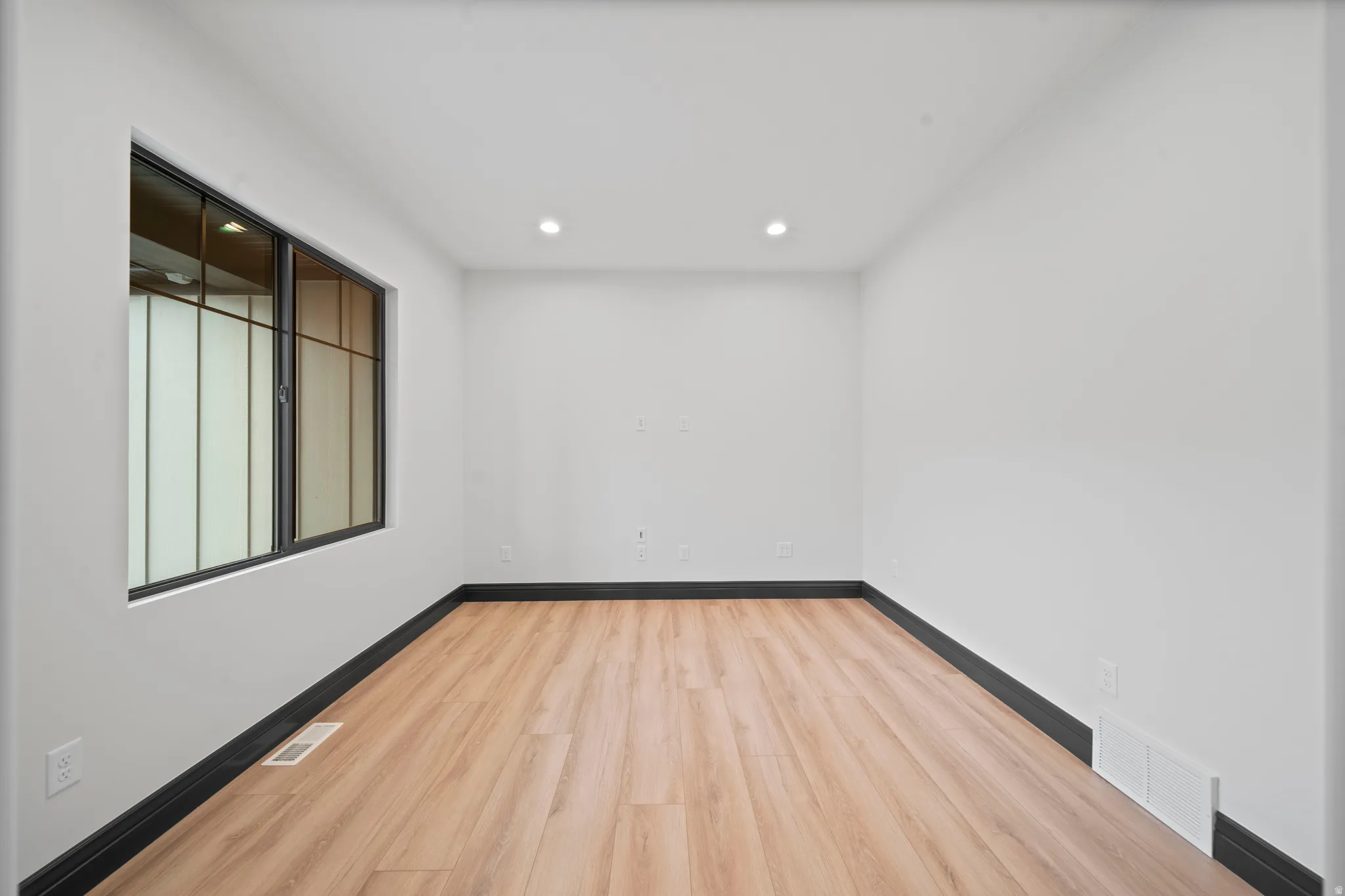 Room featuring wood-finish flooring, recessed lighting, and a large window with dark framing
