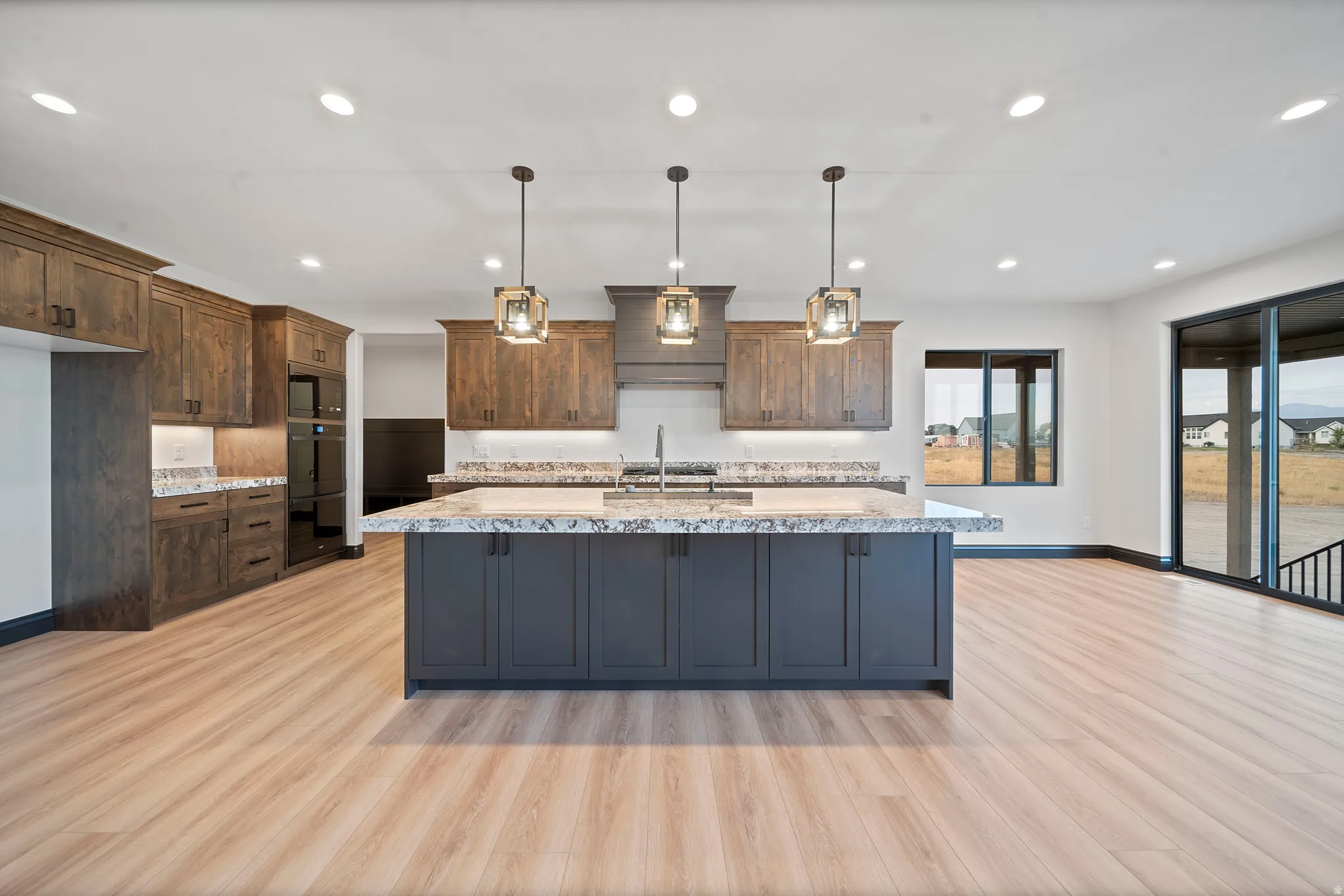 Kitchen featuring a large central island with dark cabinetry, granite-finish countertops, warm wood-finish flooring, and contemporary pendant lighting