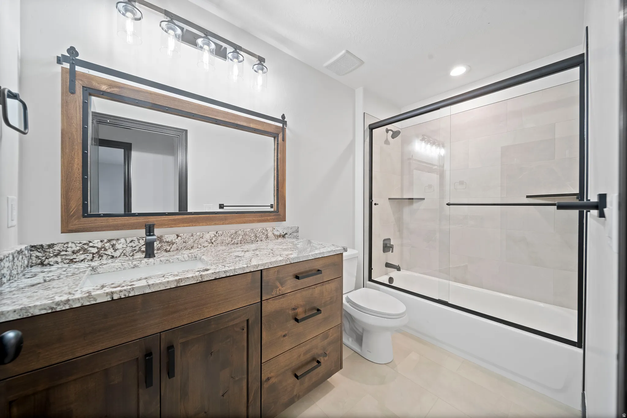 Bathroom featuring a wood-finish vanity with a granite-style countertop, undermount sink, and matte black faucet
