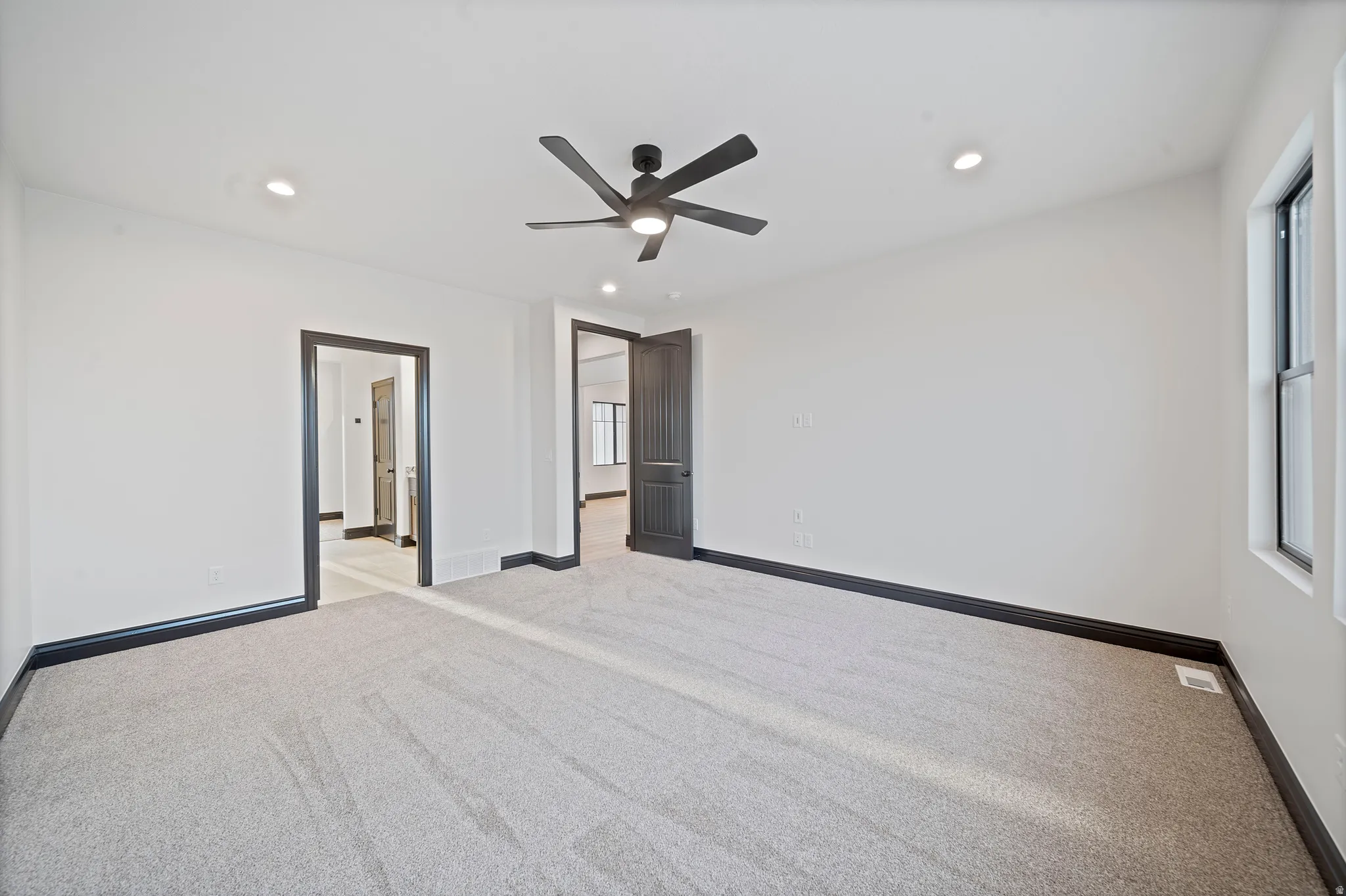Spacious room featuring light-colored carpeting, white wall finishes, and dark trim