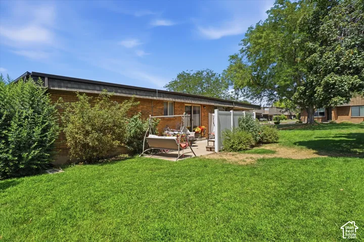 Private patio space with brick exterior, surrounded by manicured shrubs and a vibrant green lawn