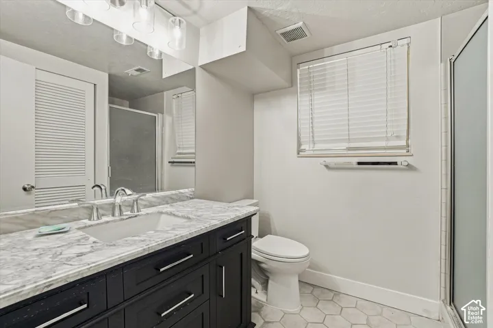 Bathroom featuring a dark wood vanity with a white countertop and undermount sink, hexagonal tile flooring, and a shower with a clear glass enclosure