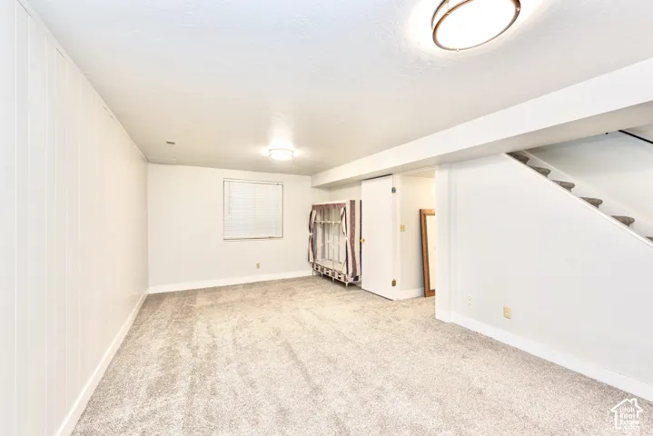 Carpeted flooring, paneled wall detail, recessed window with blinds, ceiling-mounted lighting, and a visible staircase