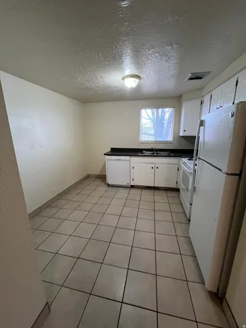 Kitchen featuring white cabinetry, dark countertops, a window, ceramic tile flooring, and white appliances