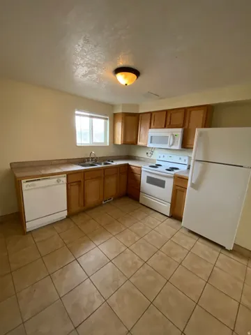 Kitchen featuring light wood cabinetry, white appliances, dual basin sink, and ceramic tile flooring