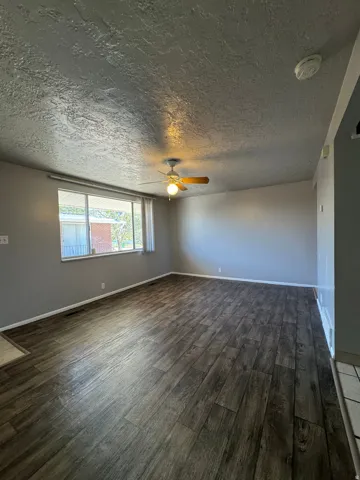 Spacious room featuring wood-finish flooring, a ceiling fan with integrated lighting, and neutral wall tones