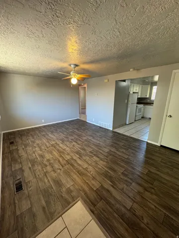 Spacious living area featuring wood-finish flooring, a ceiling fan with light fixture, and neutral wall tones