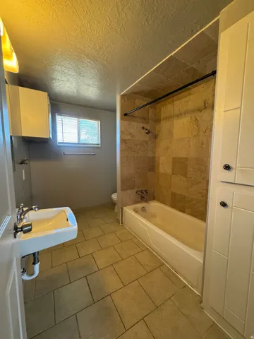 Bathroom featuring a full tub/shower combination with tile surround, a pedestal sink with chrome fixtures, and complementary tile flooring