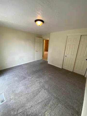 Carpeted room featuring light-toned walls, a flush-mount ceiling light fixture, a paneled interior door, and bi-fold closet doors