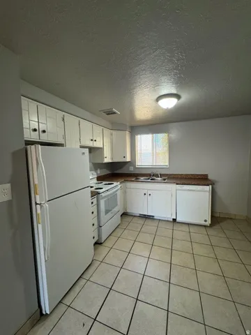 Kitchen featuring white cabinetry, light-toned tiled flooring, and a window with blinds