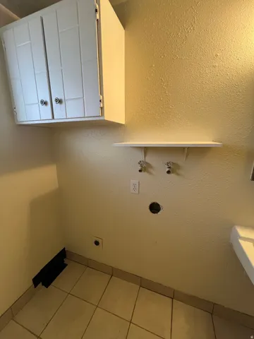 Dedicated utility area featuring overhead white cabinetry, a wall-mounted white shelf, and ceramic tile flooring