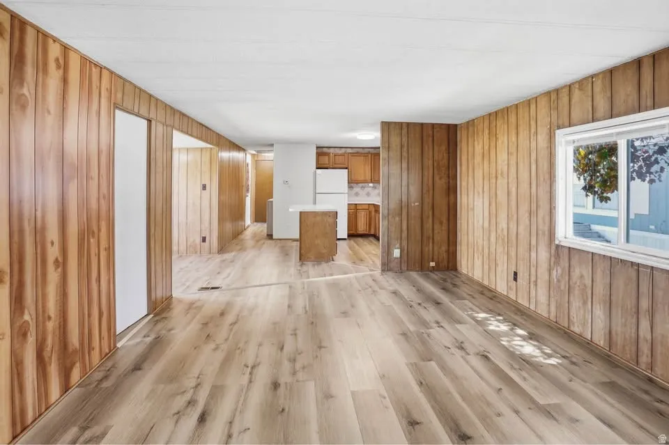 Spacious room featuring light wood-finish flooring, wood panel walls, and a white ceiling