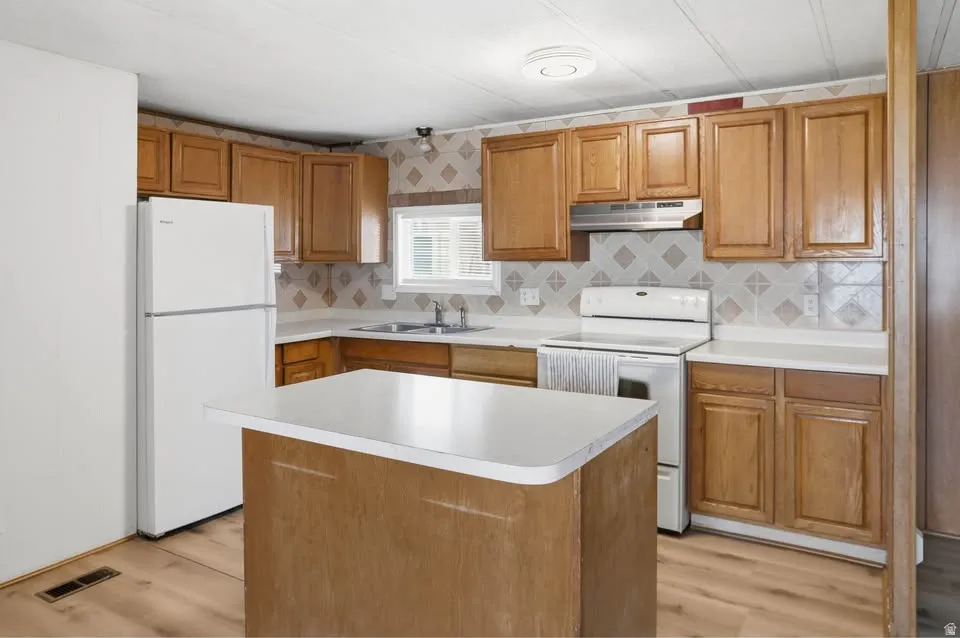 Kitchen featuring wood-finish cabinetry, white appliances, and a central island with a white countertop