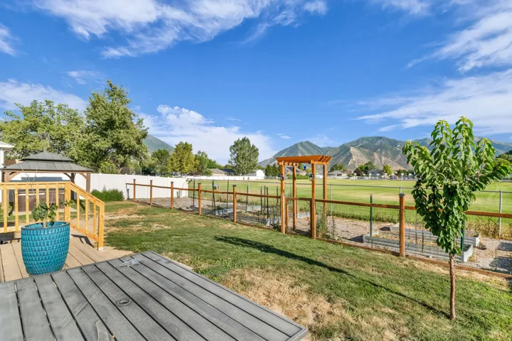 Expansive backyard featuring a multi-level wood deck, a built-in gazebo, mountain views, fencing, a garden arbor, and raised garden beds