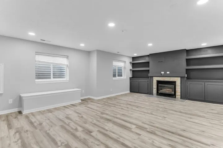 Spacious room featuring wood-finish flooring, recessed lighting, and a stone-surround fireplace and lots of built in shelving