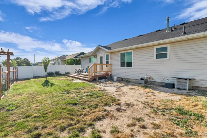 Expansive backyard featuring a wood deck, white vinyl fencing, and a small tree