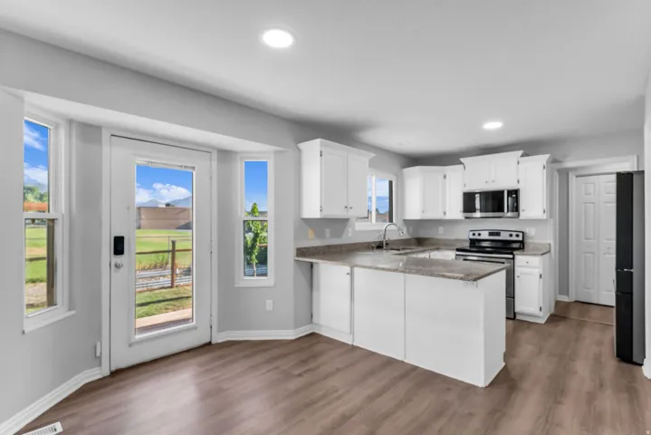 Kitchen featuring white cabinetry, granite countertops, stainless steel appliances, a doubl sink, and wood-finish flooring