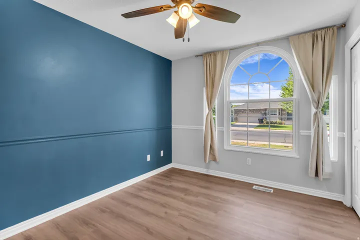Room featuring wood-finish flooring, a decorative arched window, and a ceiling fan with integrated lighting