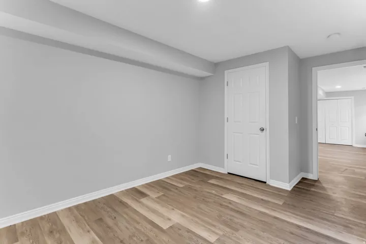 Room featuring light wood-finish flooring, light gray walls, white baseboards, and a white panel door