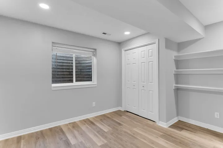 Finished room featuring wood-finish flooring, recessed lighting, a window with blinds, bi-fold closet doors, and integrated shelving