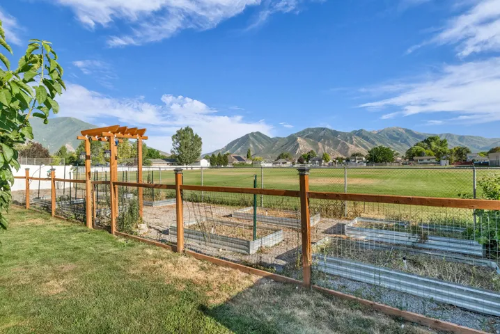 Landscaped backyard featuring a dedicated garden area with multiple raised beds, a wooden privacy fence, a wooden pergola, and a grassy lawn