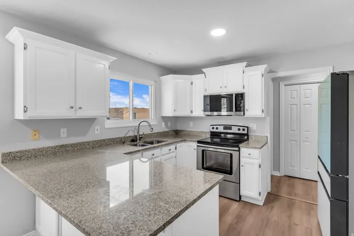Kitchen featuring white cabinetry, granite countertops, stainless steel appliances, a doubl sink, and wood-finish flooring