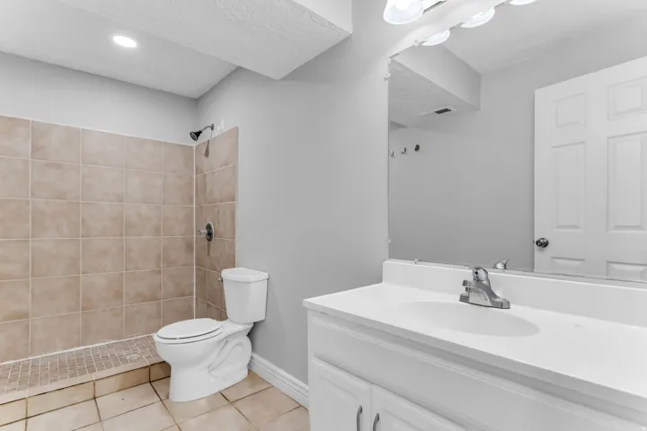 Bathroom featuring a tiled standing shower, white toilet, and a vanity with an integrated sink and mirror