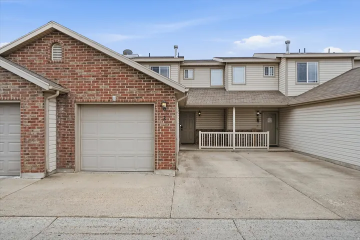 Exterior featuring brick and horizontal siding, an attached garage, a covered porch with white railing, and multiple windows
