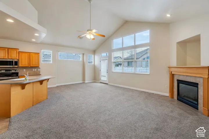 Living area featuring vaulted ceilings, large picture windows, a ceiling fan, and a fireplace with a light wood mantel and tiled surround