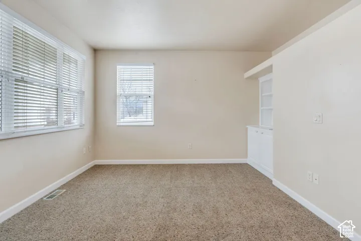 Carpeted room with neutral-toned walls, featuring a built-in white cabinetry unit with shelving