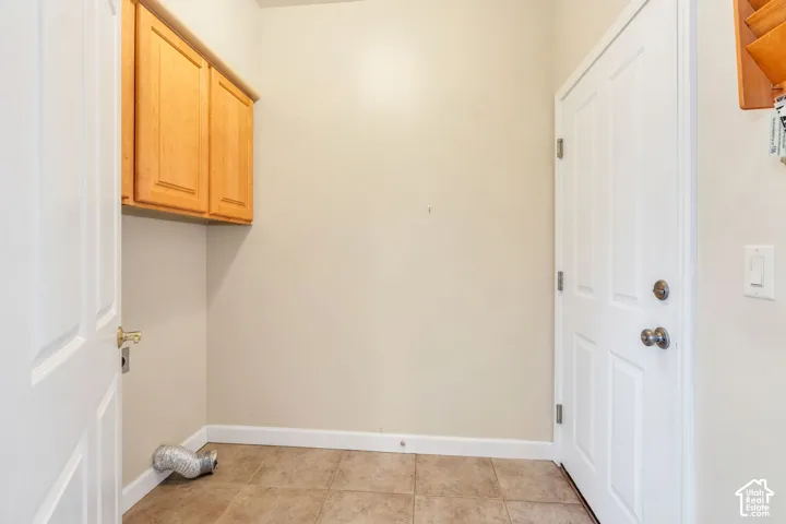 Laundry room featuring overhead wood cabinetry, neutral wall tones, and tiled flooring