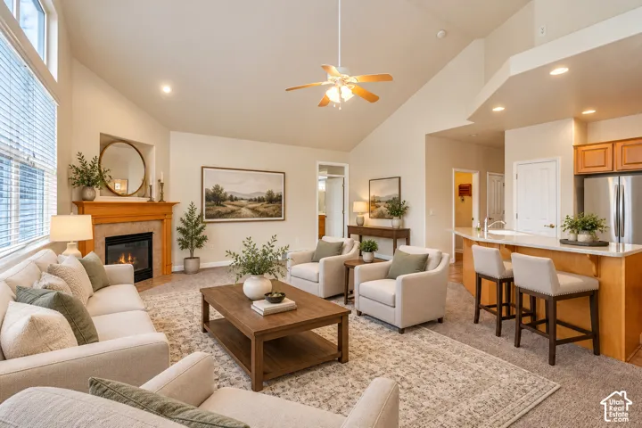 Vaulted ceilings with a ceiling fan, a fireplace with a wood mantel, a kitchen island with seating, a stainless steel refrigerator, and wood-finish cabinetry
