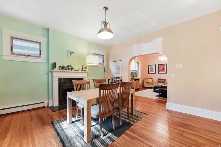 Hardwood flooring throughout, featuring a fireplace with a white mantel and dark stone surround, and an arched doorway leading to an additional space