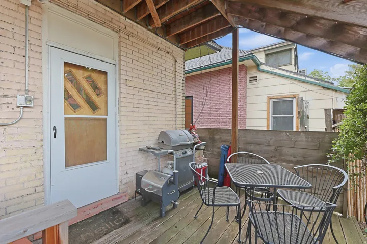 Covered outdoor deck with exposed wood rafters, featuring a light brick exterior wall and a privacy fence