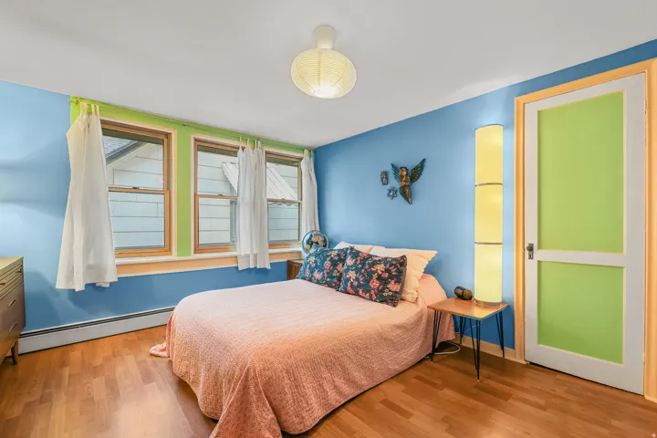Wood-finish flooring throughout, featuring a wall of three windows with trim, a ceiling-mounted light fixture, and a paneled door
