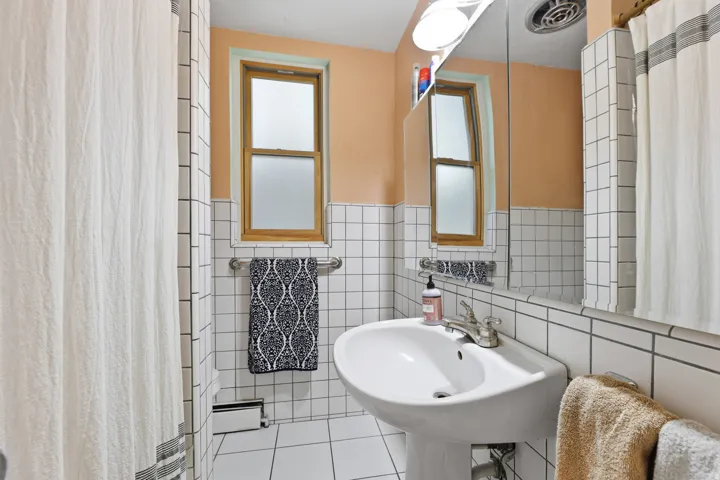 Bathroom with white square tile walls, a pedestal sink, and a mirrored medicine cabinet
