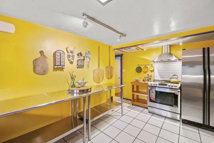 Spacious kitchen area featuring white square floor tiles, extensive stainless steel countertop space, a stainless steel range with a coordinating hood, a stainless steel refrigerator, and track lighting