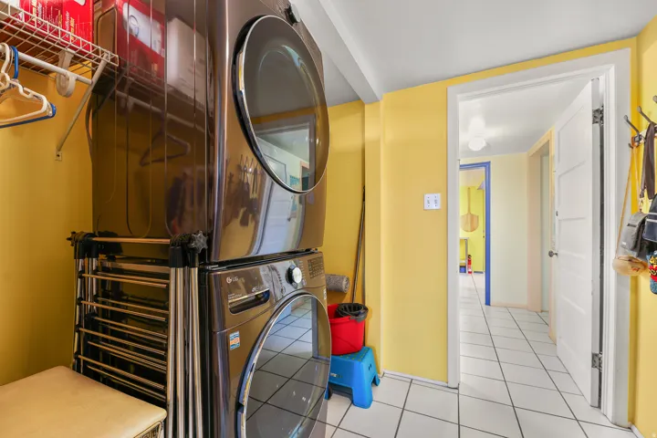 Laundry area featuring a stacked washer and dryer unit, white floor tiling, and a bright yellow wall finish