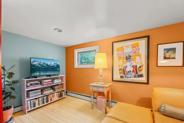 Wood-finish flooring anchors this room featuring a window with exterior views, wall-mounted baseboard heating, recessed ceiling lighting, and a built-in shelving unit