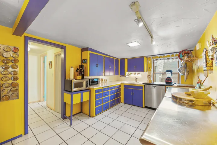 Kitchen featuring white tile flooring, purple and yellow cabinetry, a stainless steel dishwasher, and a window with natural light