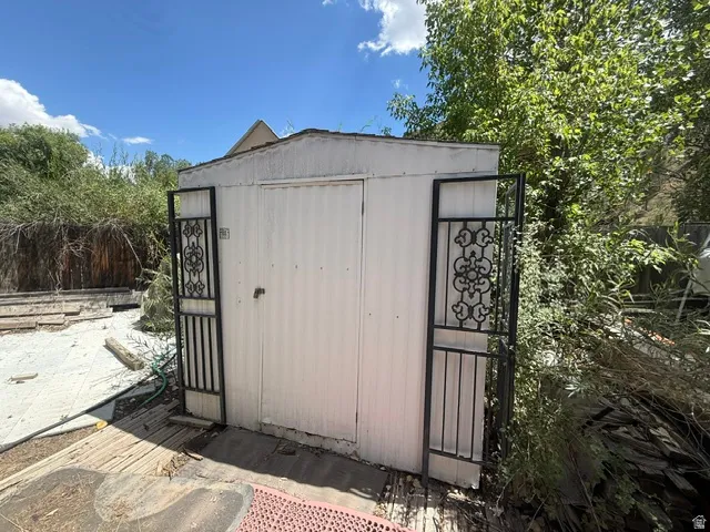 White corrugated metal shed with a flat roof and a single door, flanked by black wrought iron decorative panels