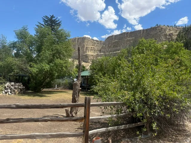 Natural wood rail fencing defines the foreground of this expansive property, featuring mature trees and a distant mountain backdrop