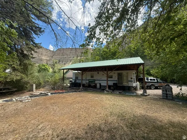 Property featuring a detached structure with a pitched metal roof, an expansive covered patio, and natural surroundings including significant rock formations