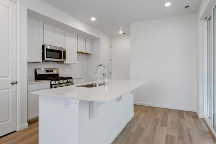 Modern kitchen featuring a central island with an undermount sink, white cabinetry, stainless steel appliances, and wood-finish flooring