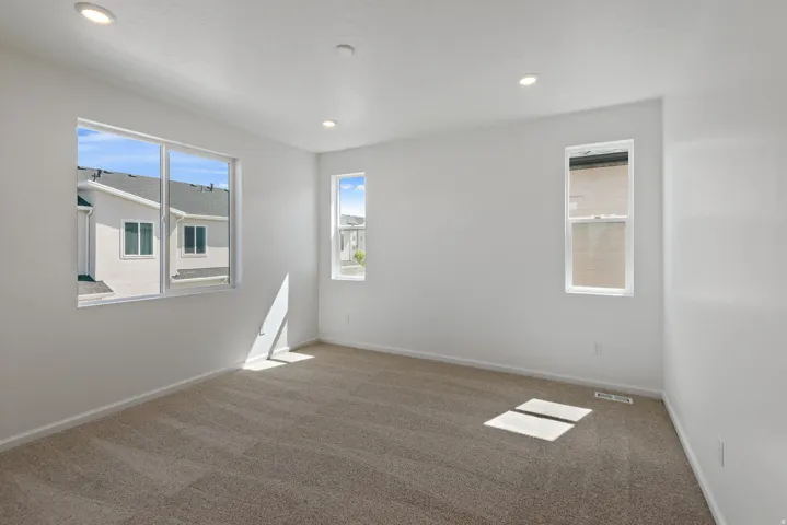 Spacious room featuring neutral carpet flooring, multiple windows, and recessed ceiling lighting